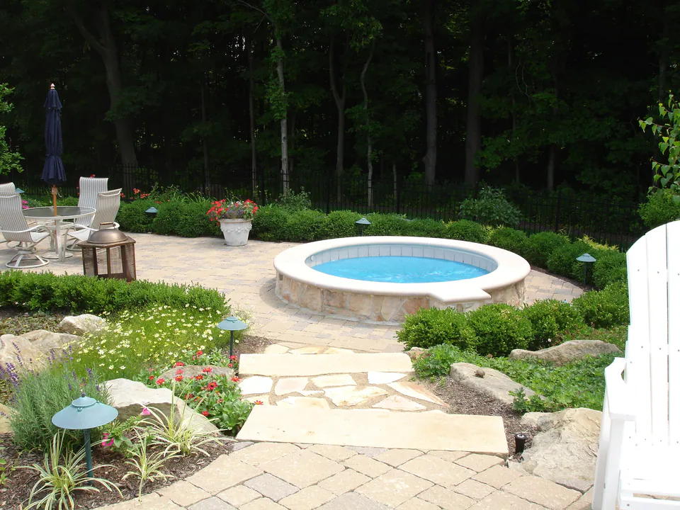 Round raised spa with a stone coping set into a paver patio surrounded by garden planting